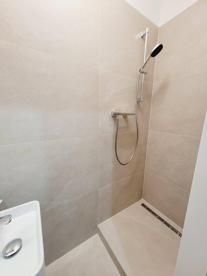 Ebenerdige Dusche im modernen Badezimmer mit beigefarbenen Fliesen und minimalistischem Design.