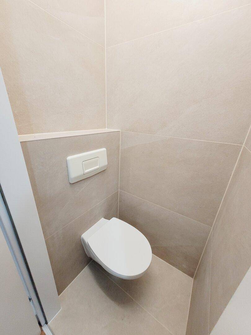 Wandhängendes WC im modernen Badezimmer mit beigefarbenen Fliesen, sauber und funktional.