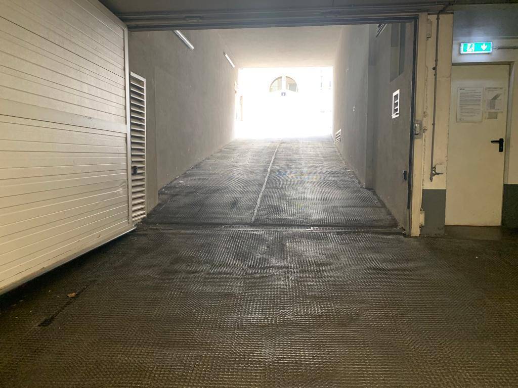 Einfahrt zur Tiefgarage mit Rampe und Rolltor, die ins Innere führt.