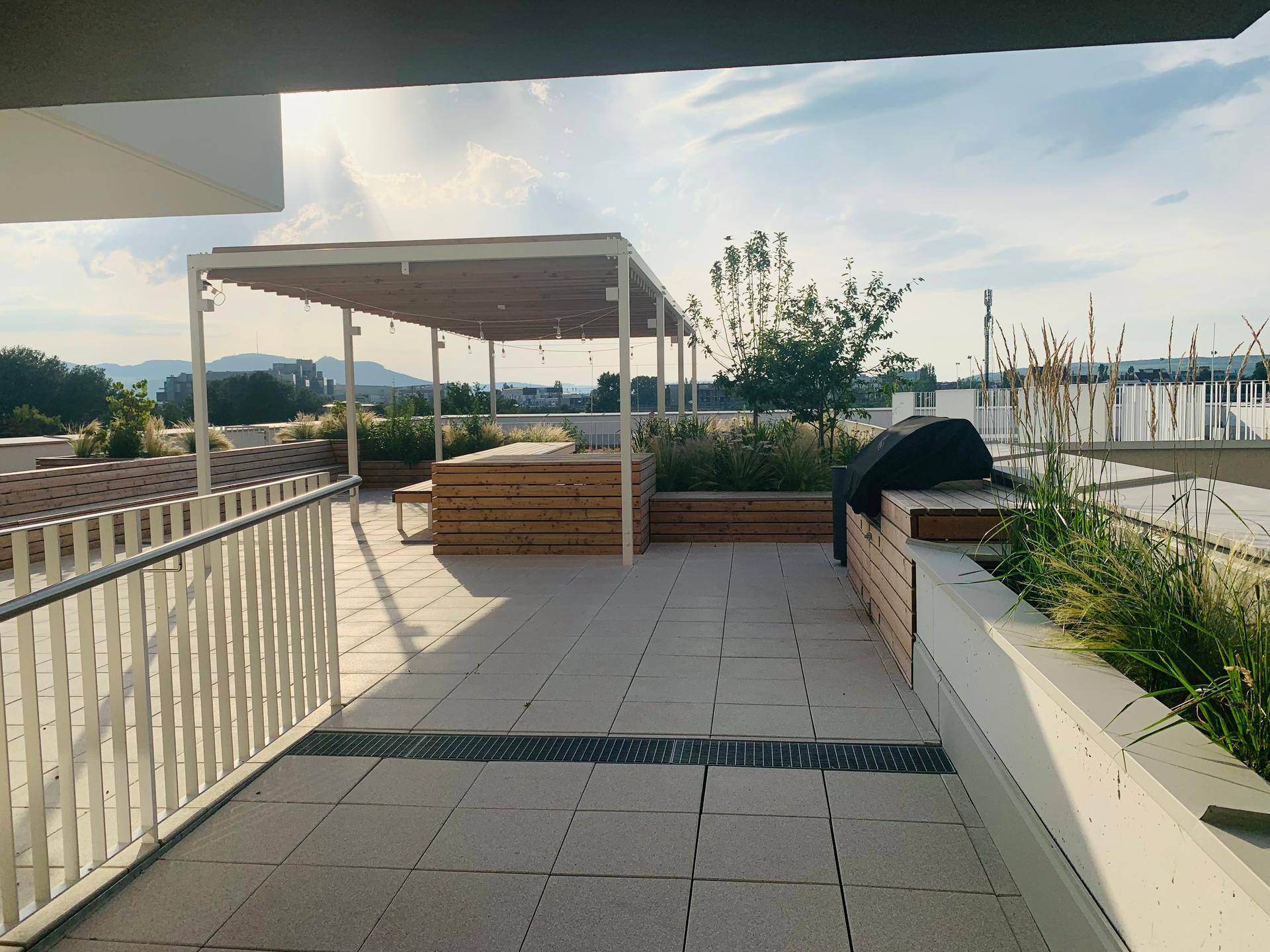 Große Dachterrasse mit Pergola, Sitzgelegenheiten und Grillbereich unter blauem Himmel.