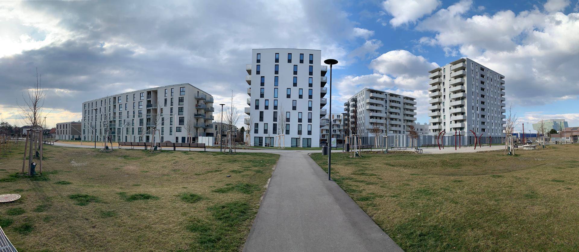 Moderne Wohngebäude in einer weitläufigen Grünanlage unter bewölktem Himmel.