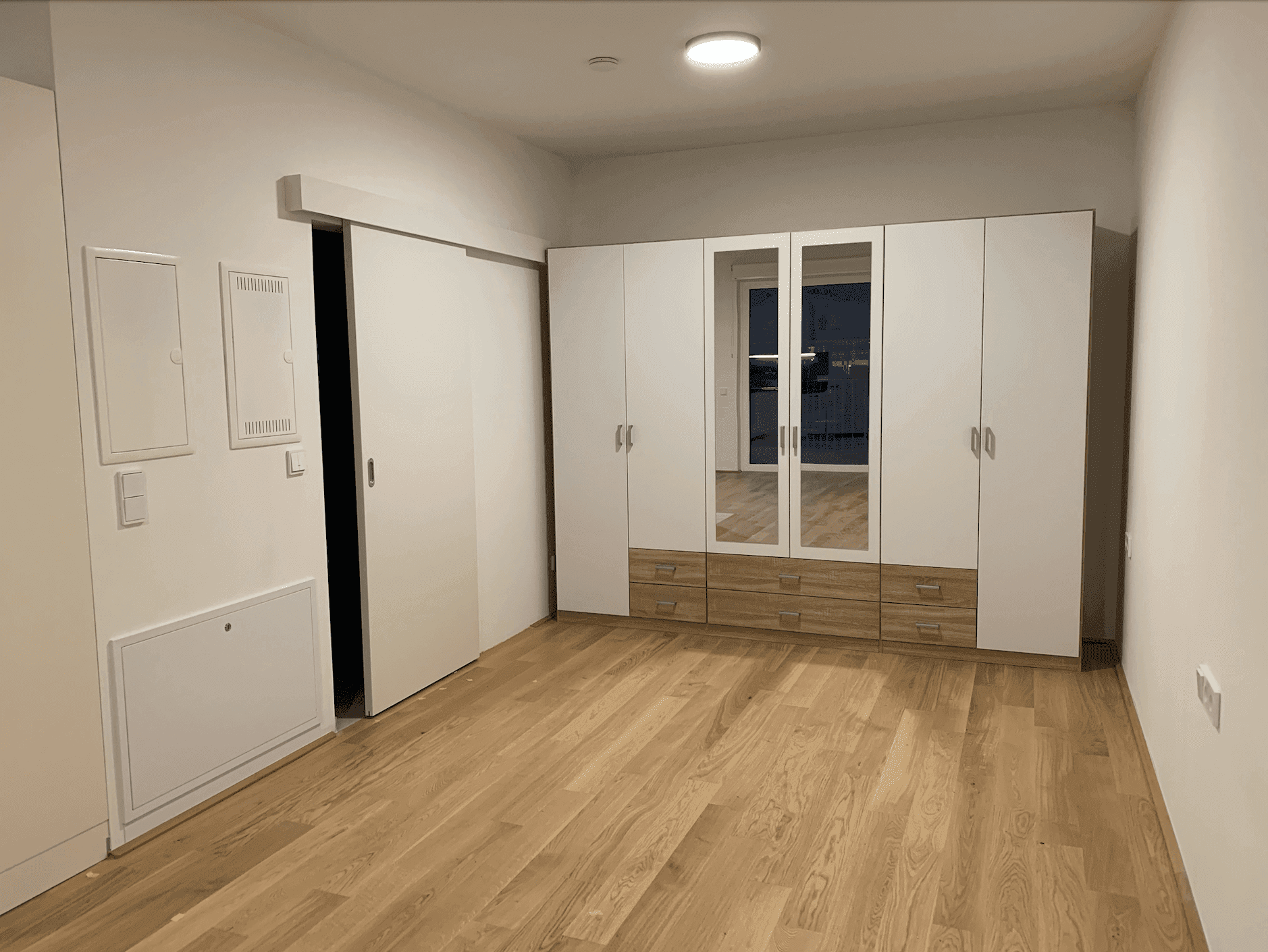 Geräumiger Wohnbereich mit Holzboden und integrierten Schränken mit Spiegelfronten.