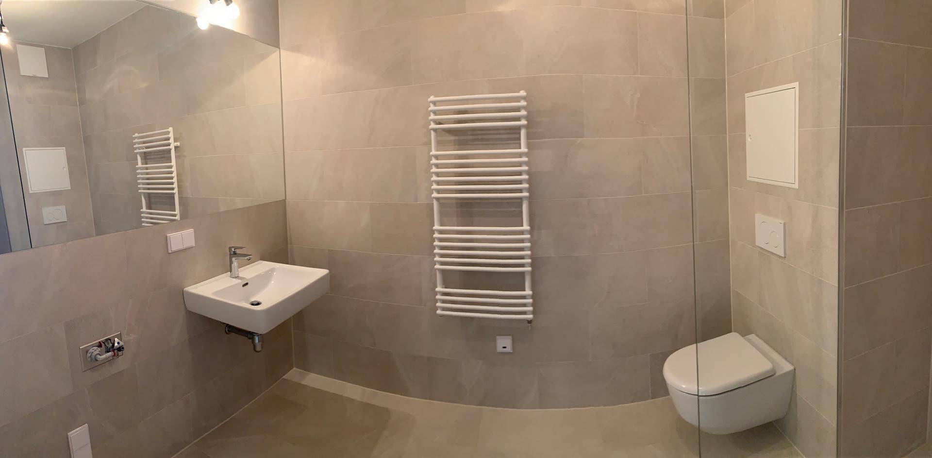 Modernes Badezimmer mit grauen Fliesen, Waschbecken, Toilette und beheiztem Handtuchhalter.