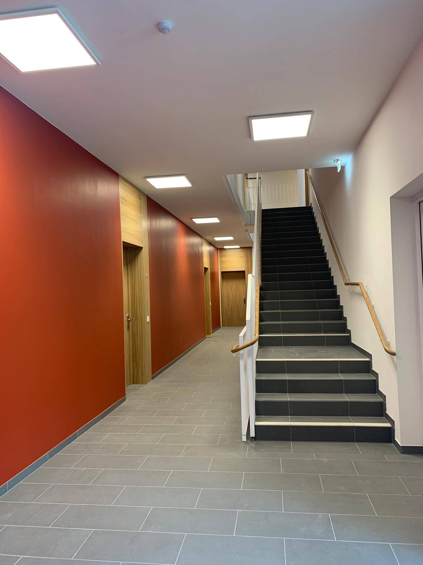 Geräumiger Flur mit Treppenaufgang, roten Wänden und modernen Beleuchtungselementen.