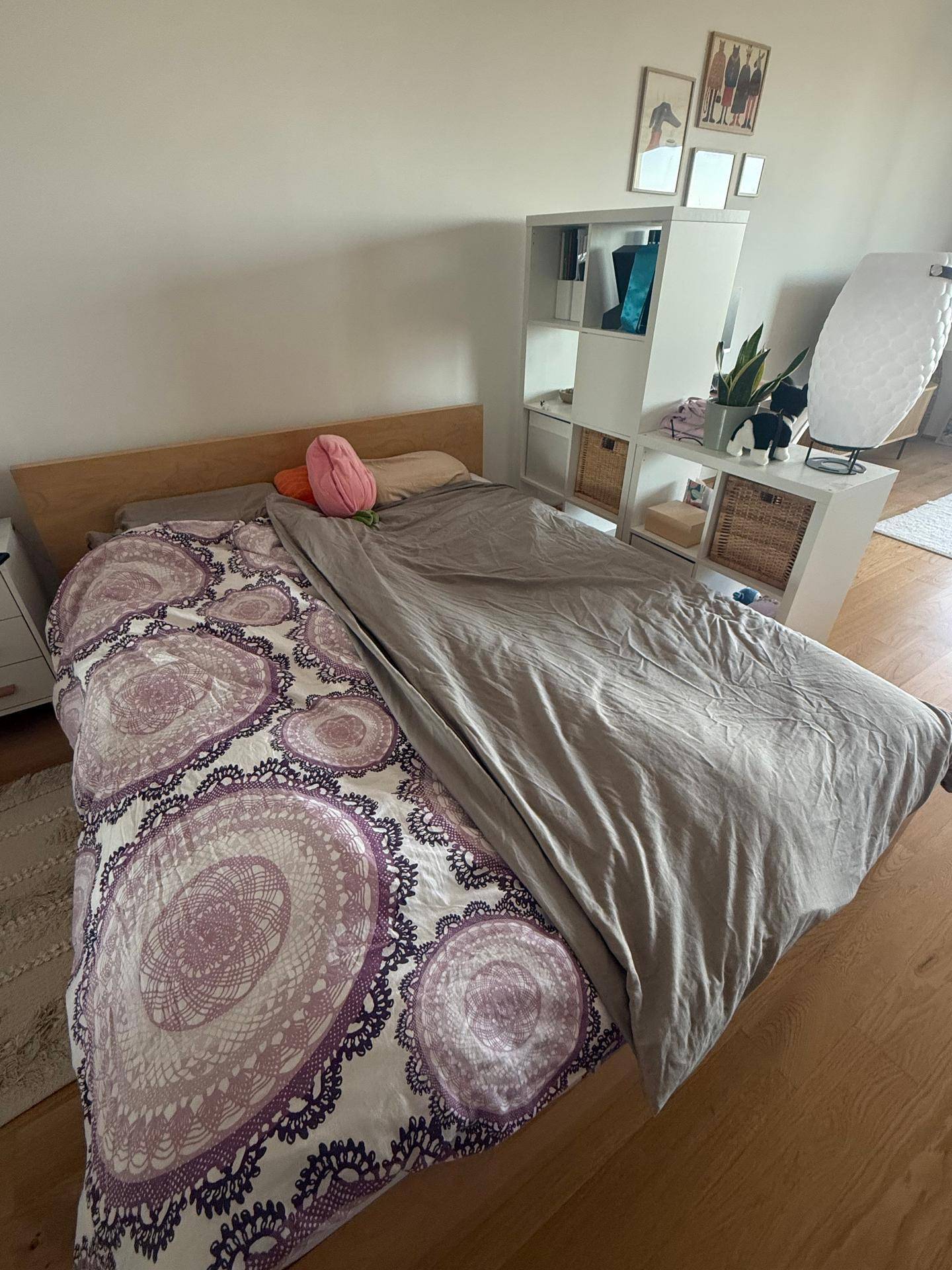 Helles Schlafzimmer mit Holzboden, einem großen Bett und einem praktischen Regal für Stauraum.