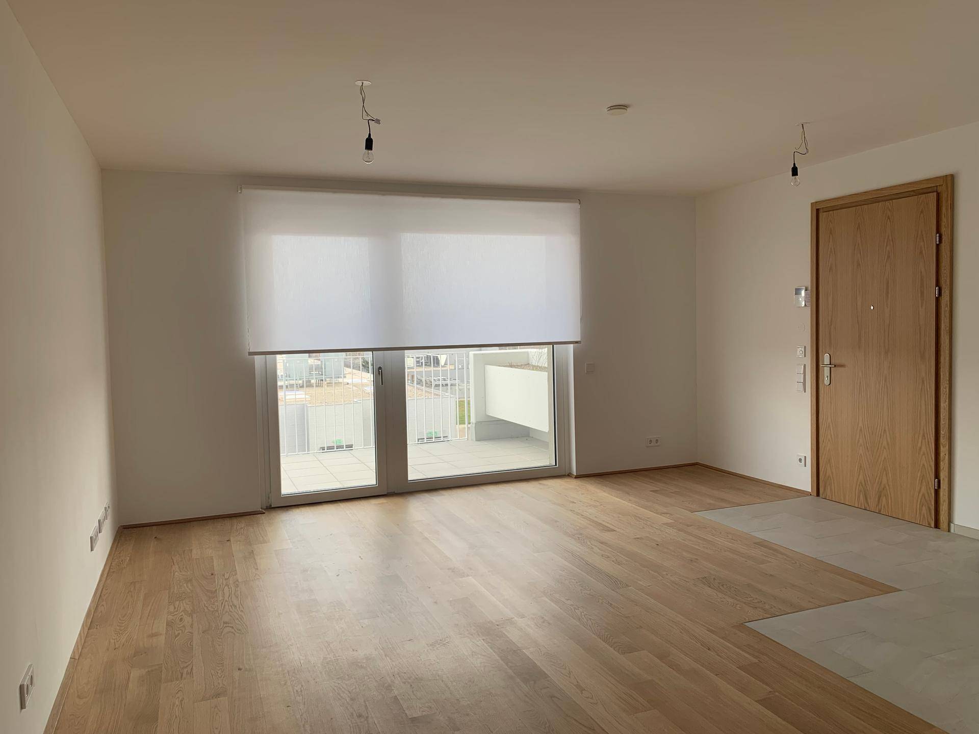 Heller Wohnraum mit Holzboden, großen Fenstern und Zugang zum Balkon.