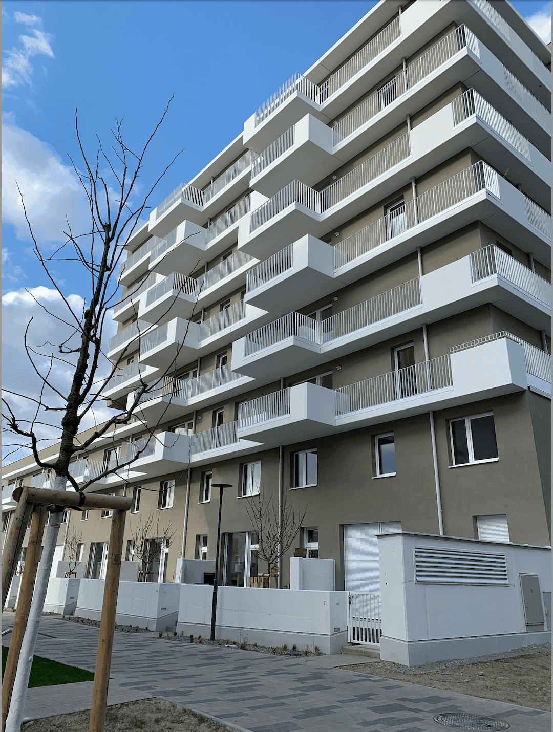 Fassade eines modernen Wohngebäudes mit zahlreichen Balkonen und klarem Himmel.