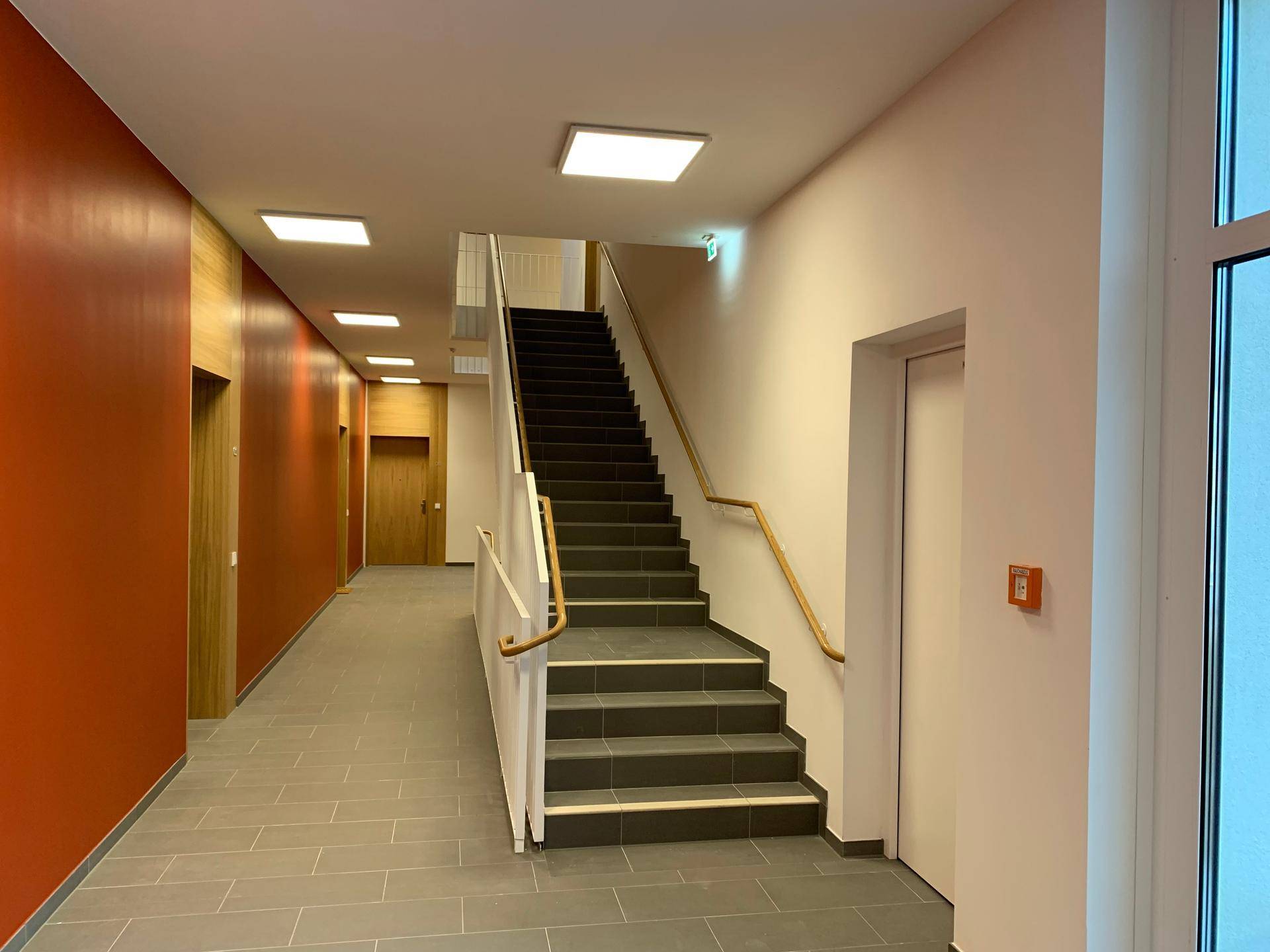 Helles Treppenhaus mit modernen Fliesen und Holzgeländer in einem Neubau.