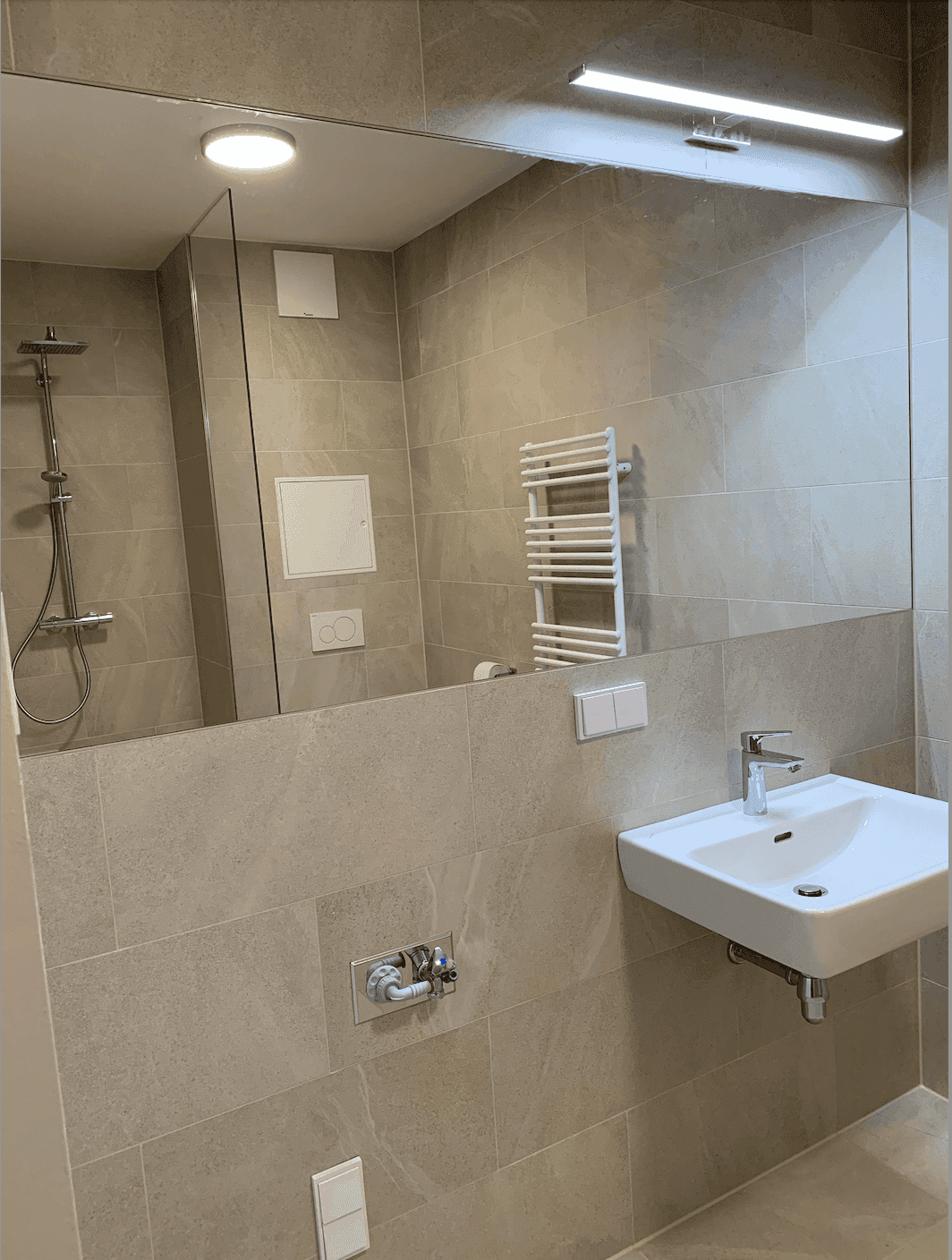 Modernes Badezimmer mit großem Spiegel, Waschbecken und Duschbereich.
