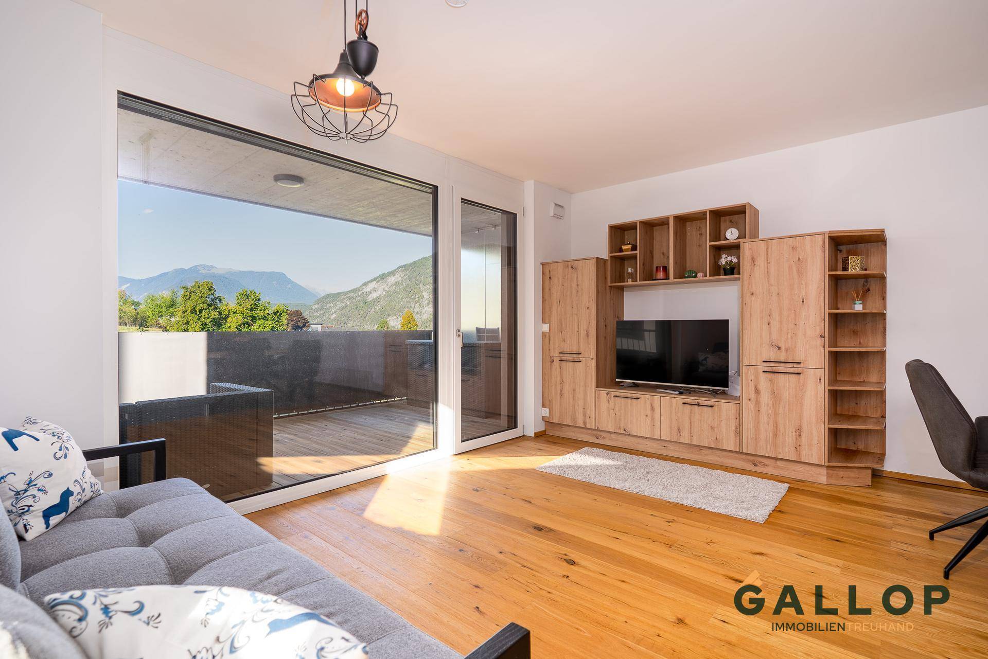 Helles Wohnzimmer mit Holzboden, Medienwand und großem Fenster mit Bergblick.