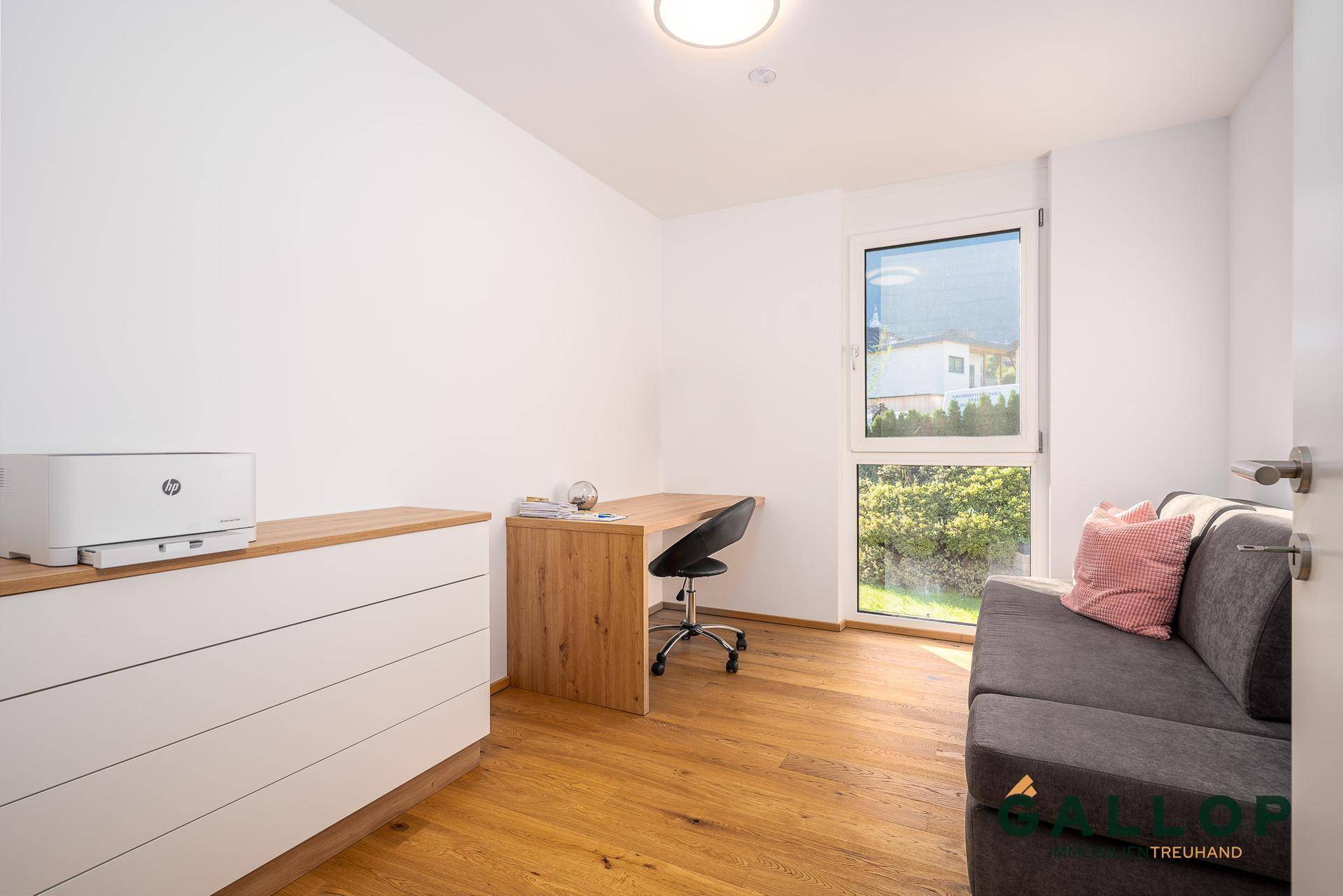 Ruhiges Arbeitszimmer mit Holzboden, Schreibtisch und Fenster mit Blick ins Grüne.