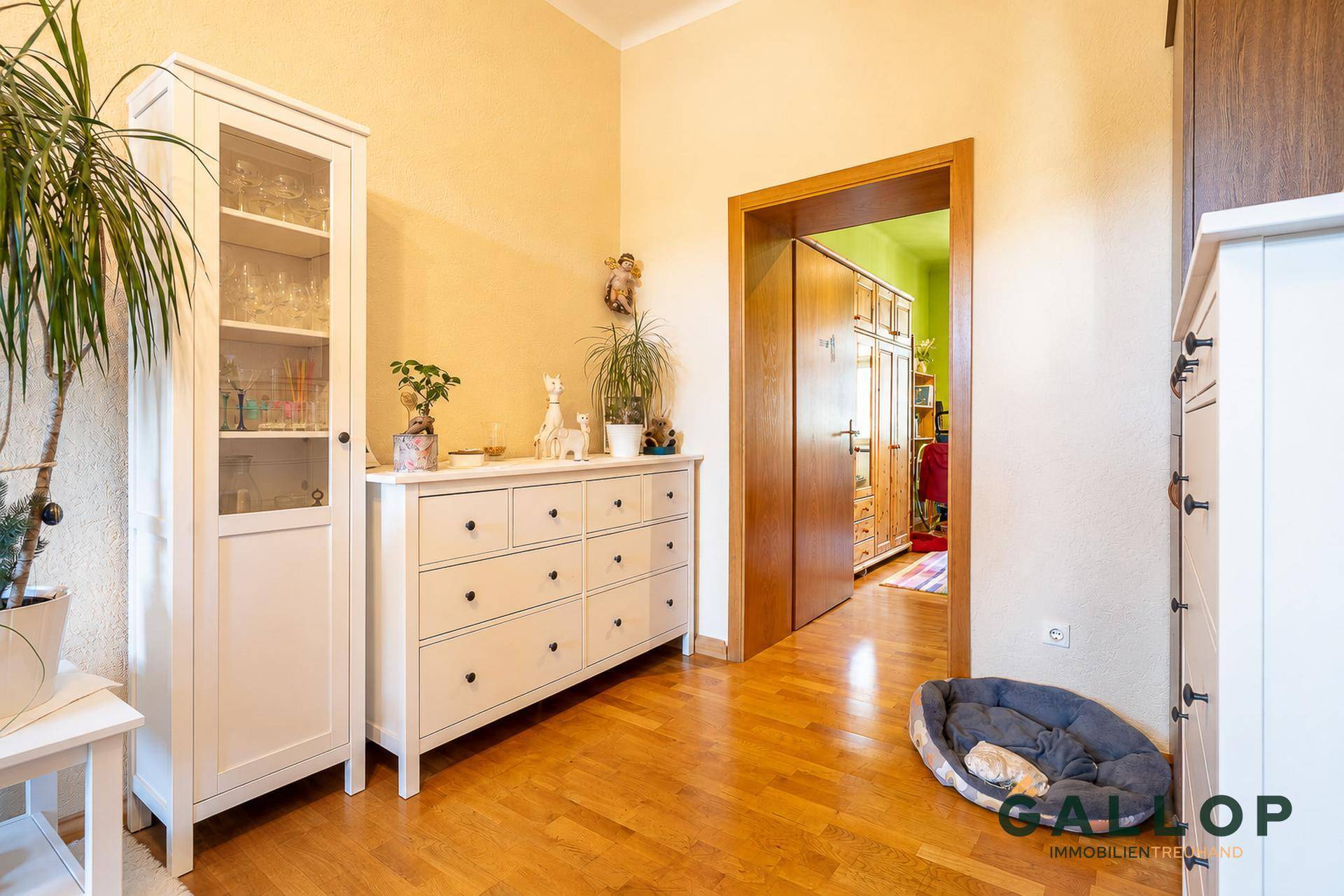 Flur mit Kommode, Vitrine und Blick in ein angrenzendes Zimmer mit Holzboden.