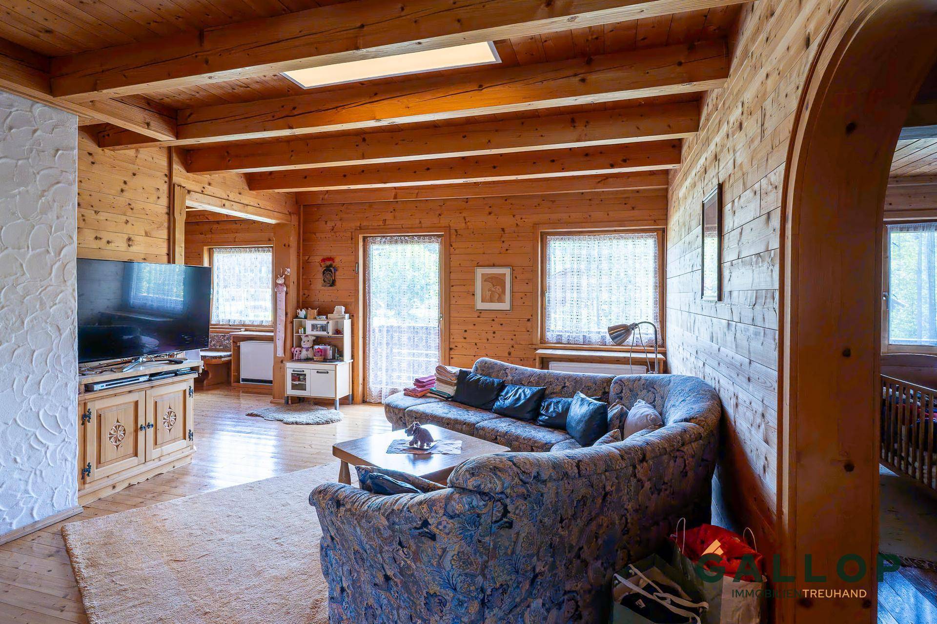 Rustikales Wohnzimmer mit Holzwänden, Holzbalkendecke und gemütlicher Sitzecke.