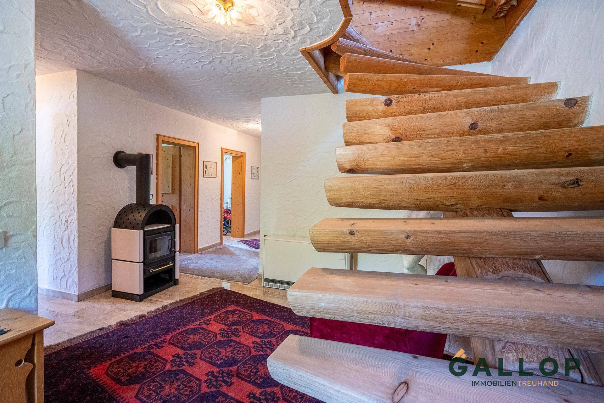 Heller Flur mit massiver Holztreppe, modernem Kaminofen und Zugang zu weiteren Räumen.