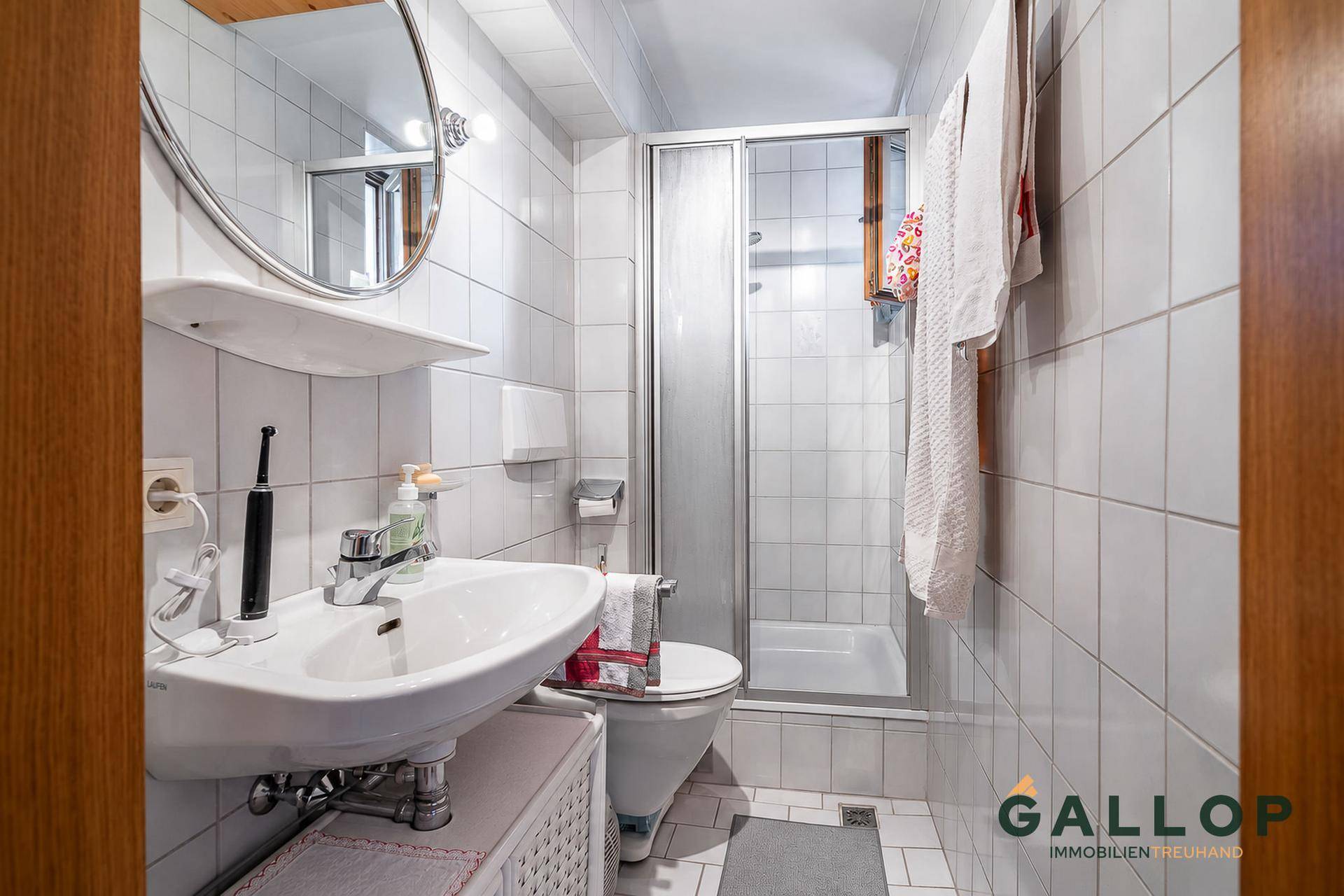 Funktionales Badezimmer mit Dusche, WC, Waschbecken und weißen Fliesen an Wänden und Boden.