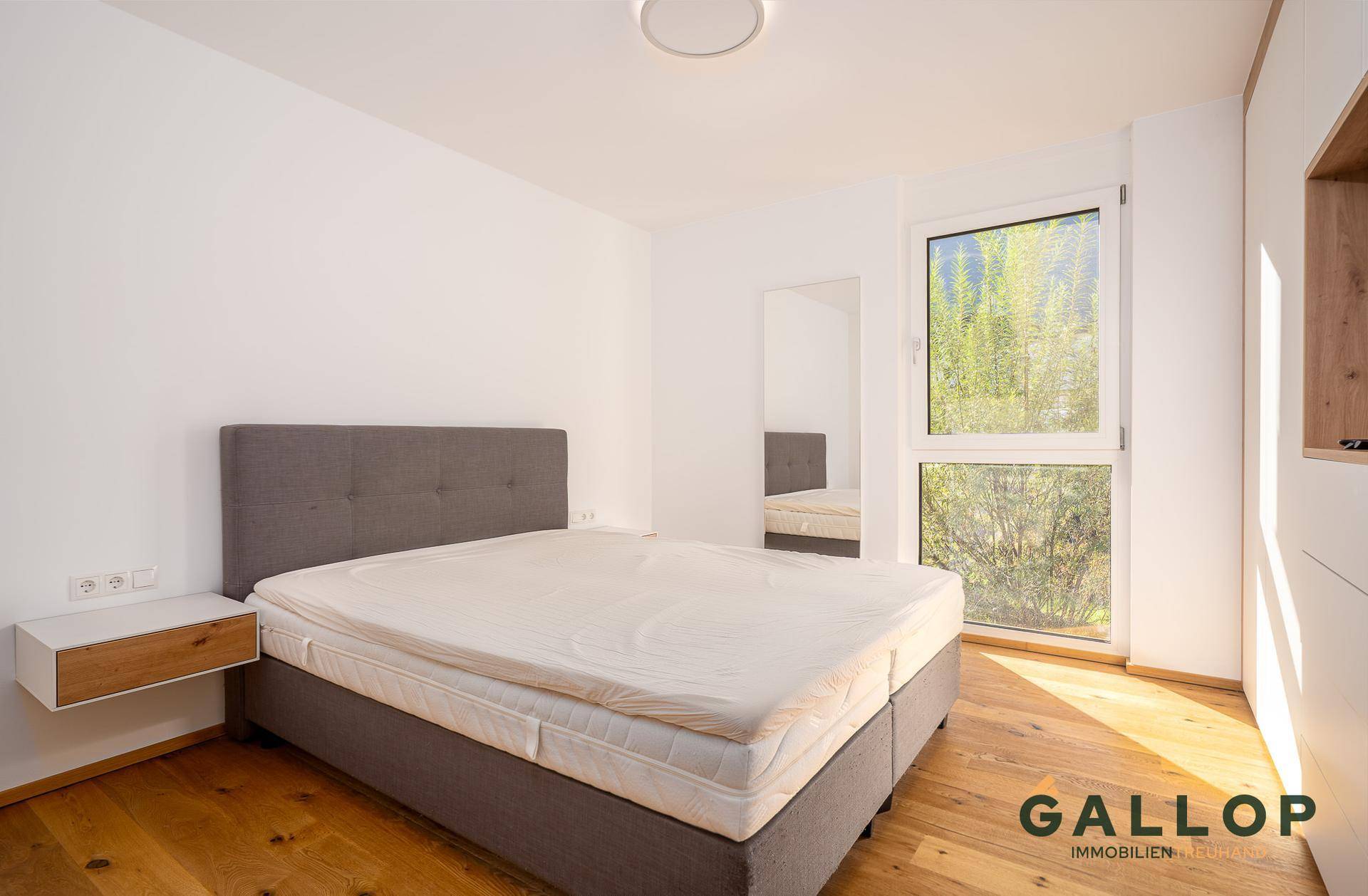 Helles Schlafzimmer mit Holzboden, großem Bett und Fenster mit Blick ins Grüne.