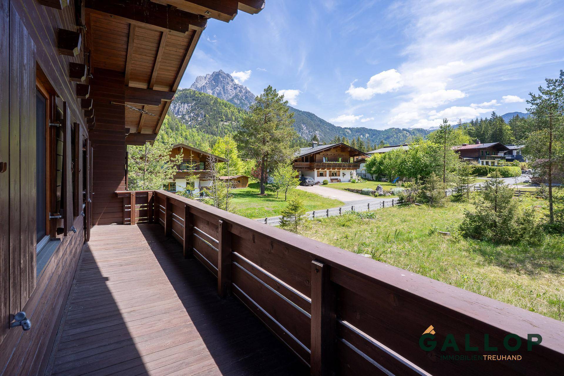 Geräumiger Holzbalkon mit Blick auf die umliegende Berglandschaft und grüne Wiesen.