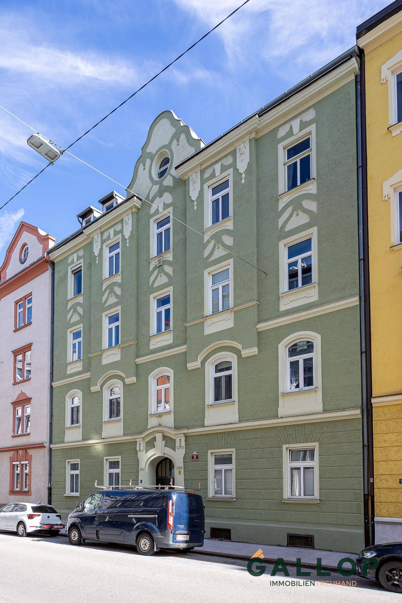 Historisches Gebäude mit grüner Fassade und traditionellen Fenstern in städtischer Umgebung.