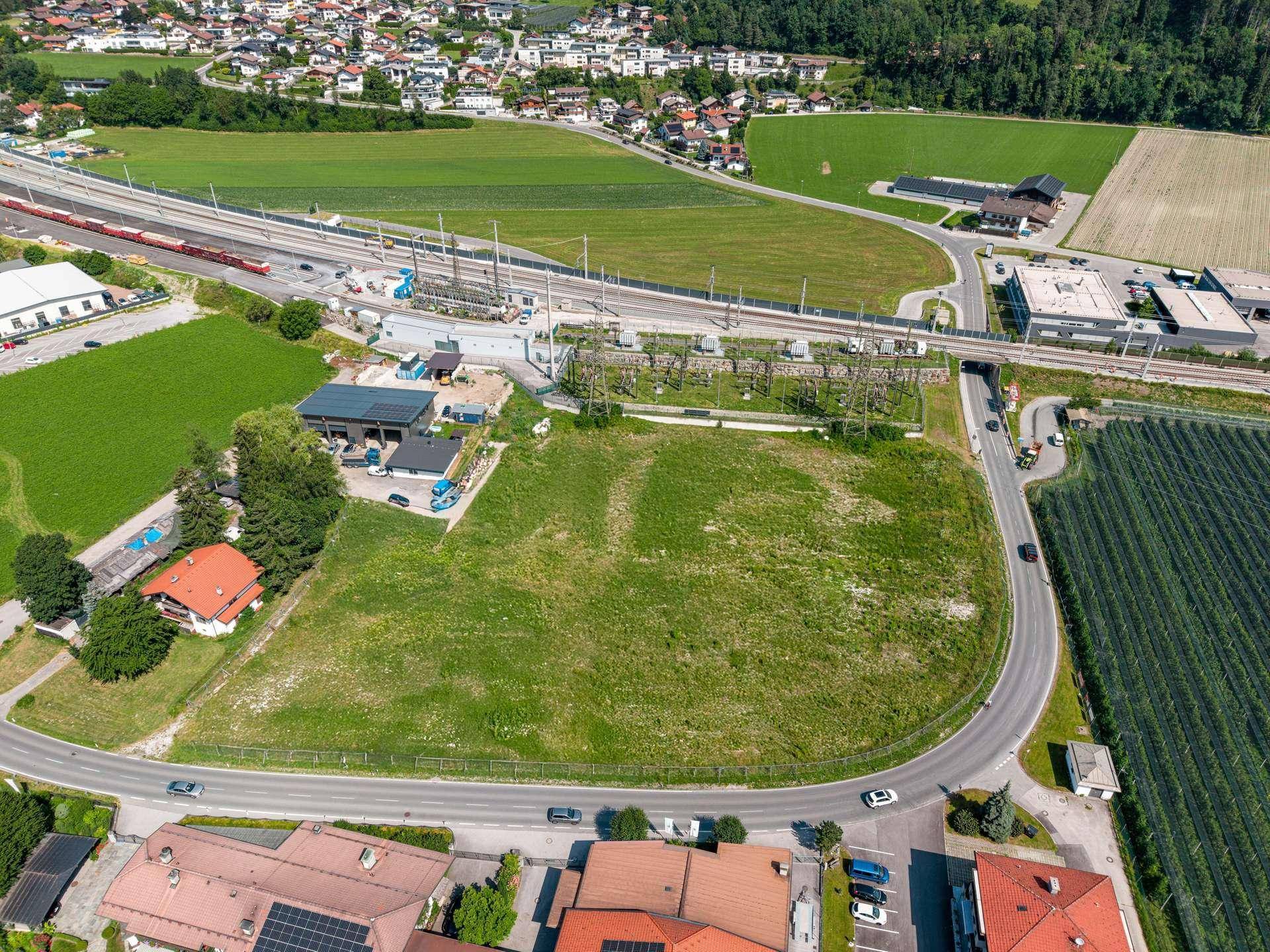 Übersichtliche Luftaufnahme eines weitläufigen grünen Grundstücks mit angrenzenden Straßen und Bahnanlagen.