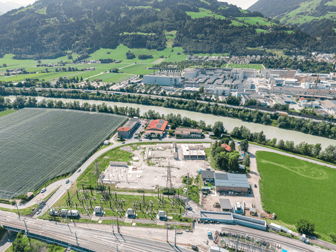Weitläufige Luftaufnahme einer ländlichen Gegend mit Fluss, Industriegebäuden und einer Umspannstation.
