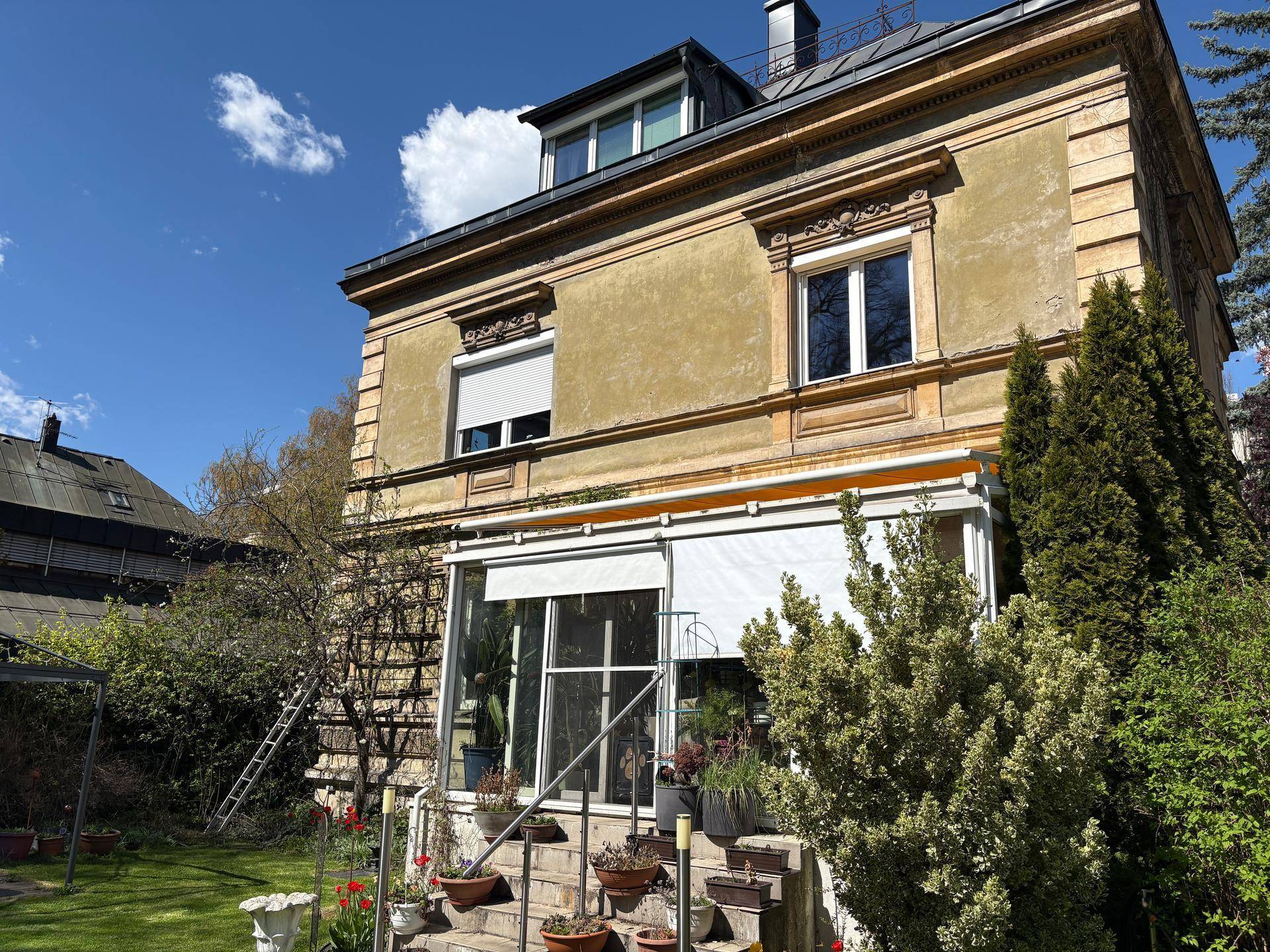 Rückseite des Gebäudes mit Wintergarten, Terrasse und gepflegtem Gartenbereich.