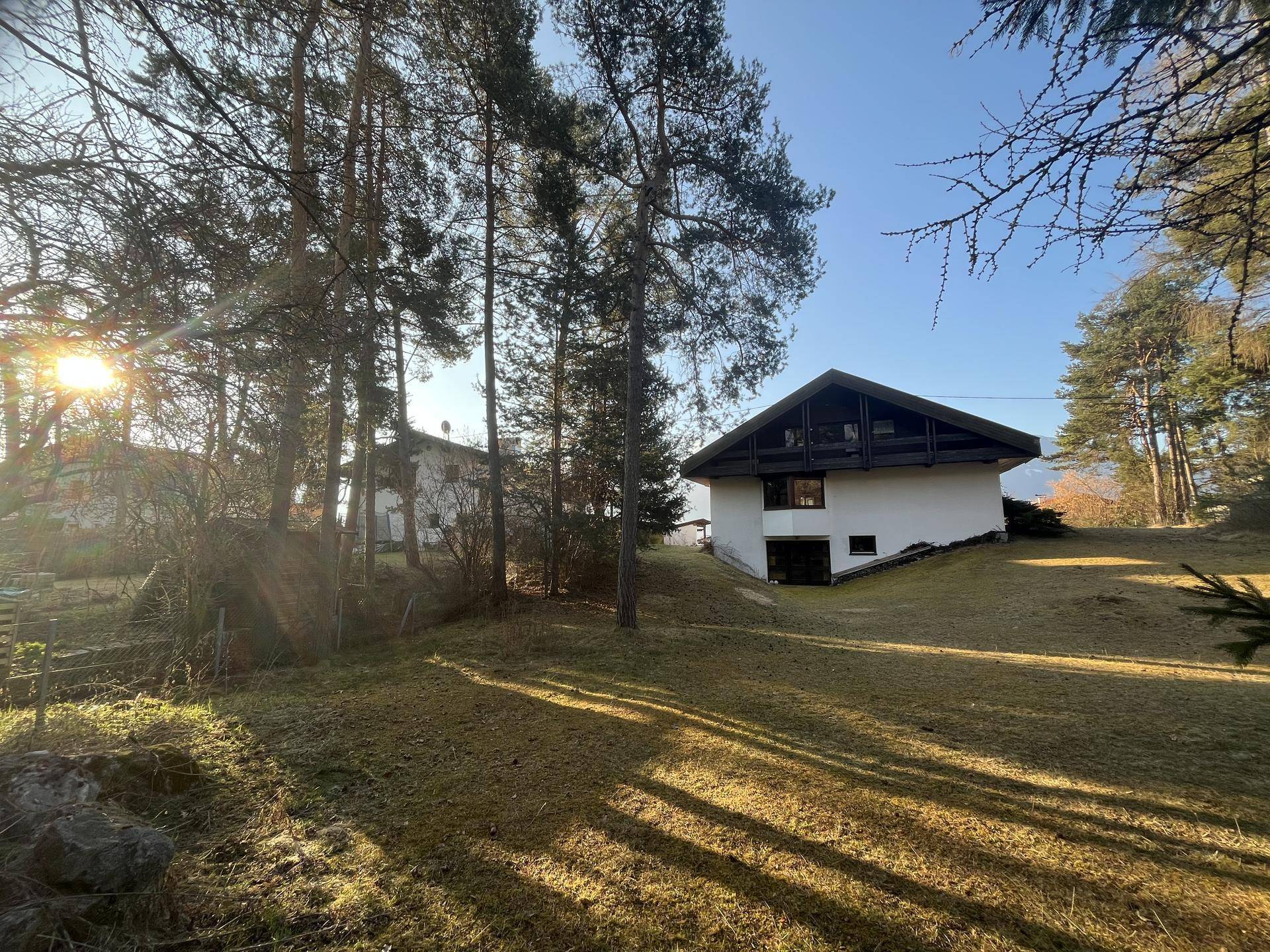 Seitenansicht des Hauses mit großem Rasenbereich und hohen Bäumen, die viel Schatten spenden, bei Sonnenschein.