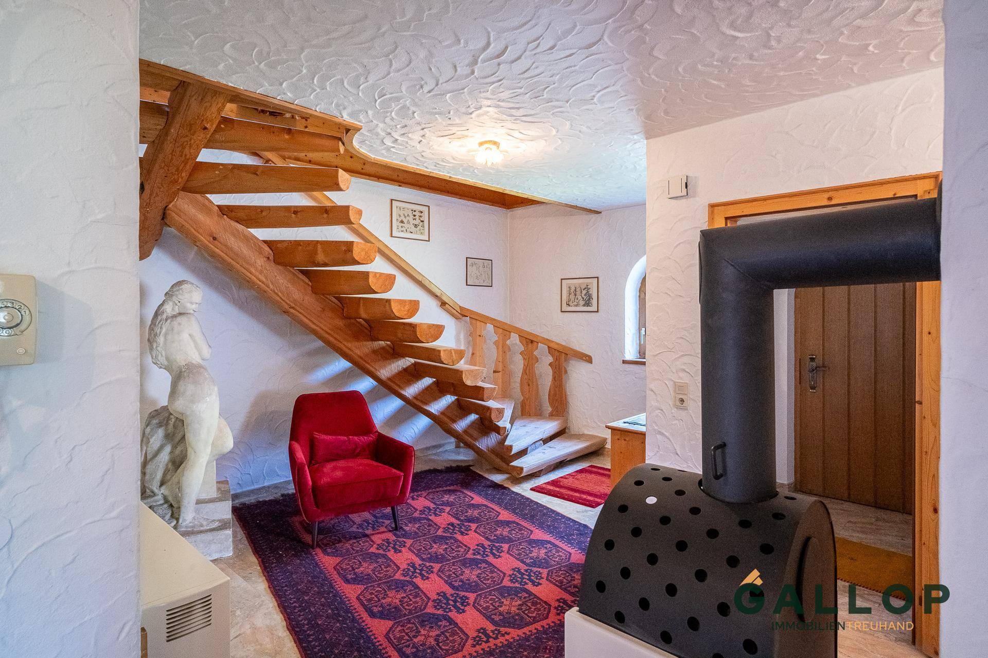 Gemütlicher Eingangsbereich mit rustikaler Holztreppe, Kaminofen und dekorativer Stuckdecke.