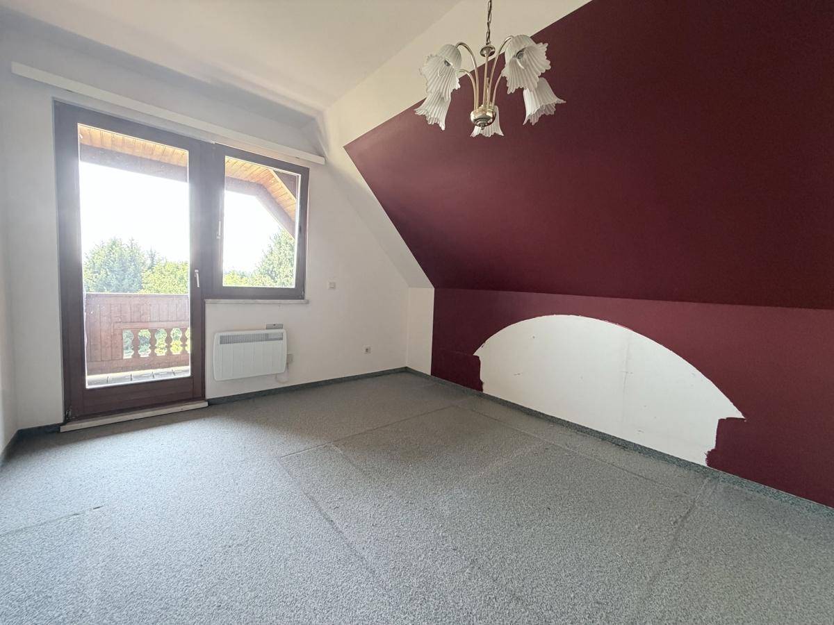 Schlafzimmer im Dachgeschoss mit Balkonzugang und farbiger Akzentwand, bietet viel Potenzial.