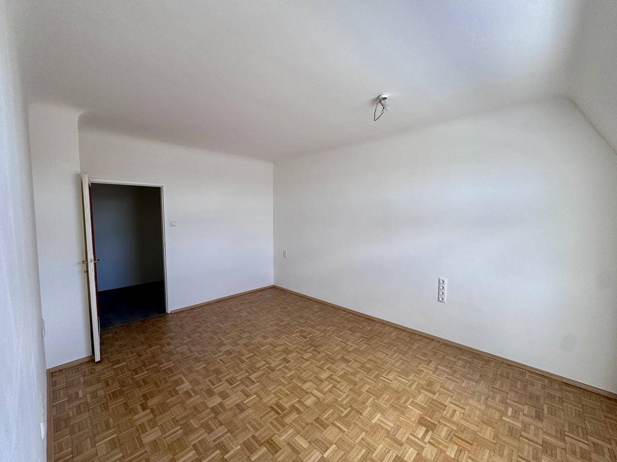 Leeres Zimmer mit Fischgrätparkettboden und weißen Wänden, bereit zur Einrichtung.