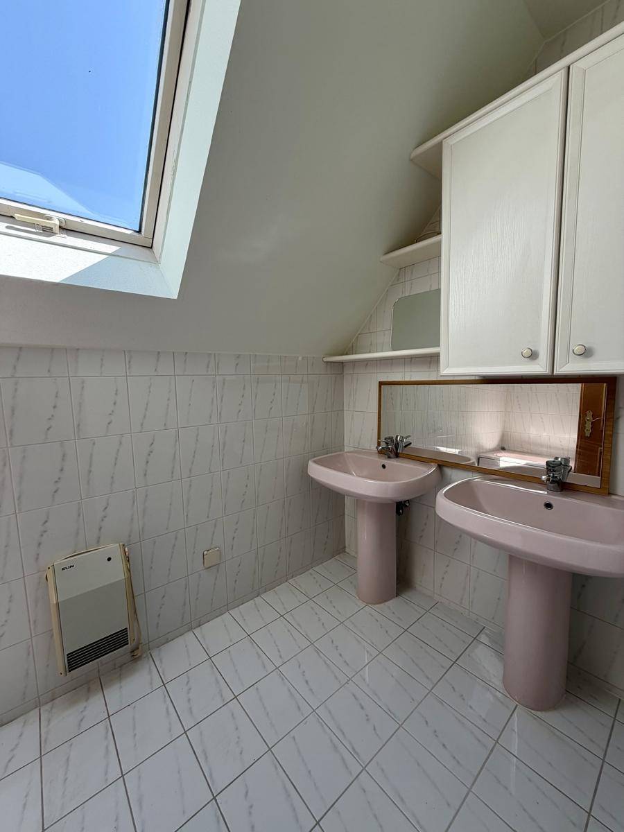 Dachgeschoss-Badezimmer mit zwei Waschbecken und Dachfenster, in einem älteren Design.