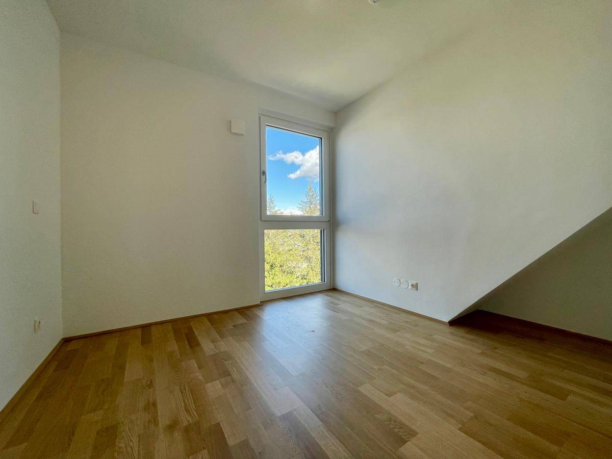 Leeres Zimmer mit Parkettboden, weiß gestrichenen Wänden und einem hohen Fenster.