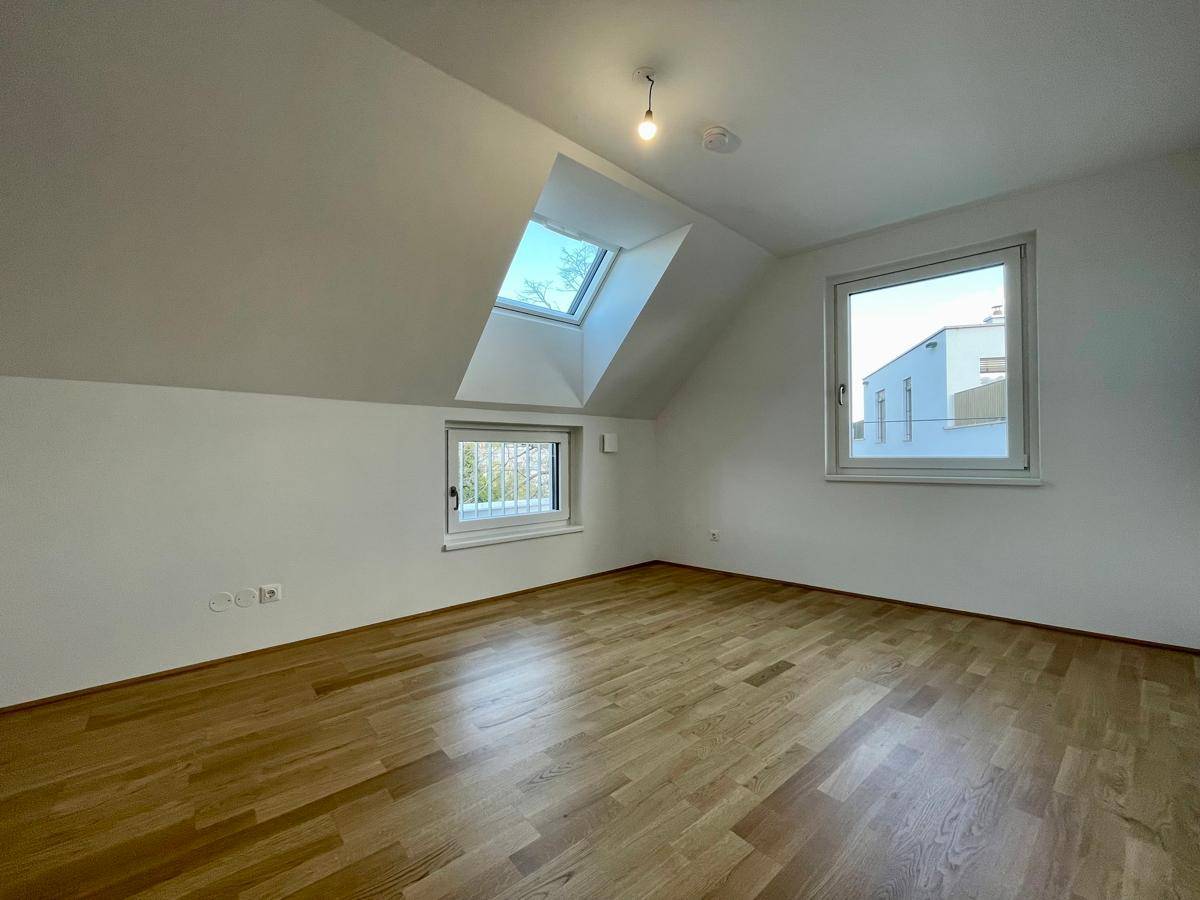 Helles Zimmer mit Holzparkettboden, Dachfenster und Blick auf die Umgebung.