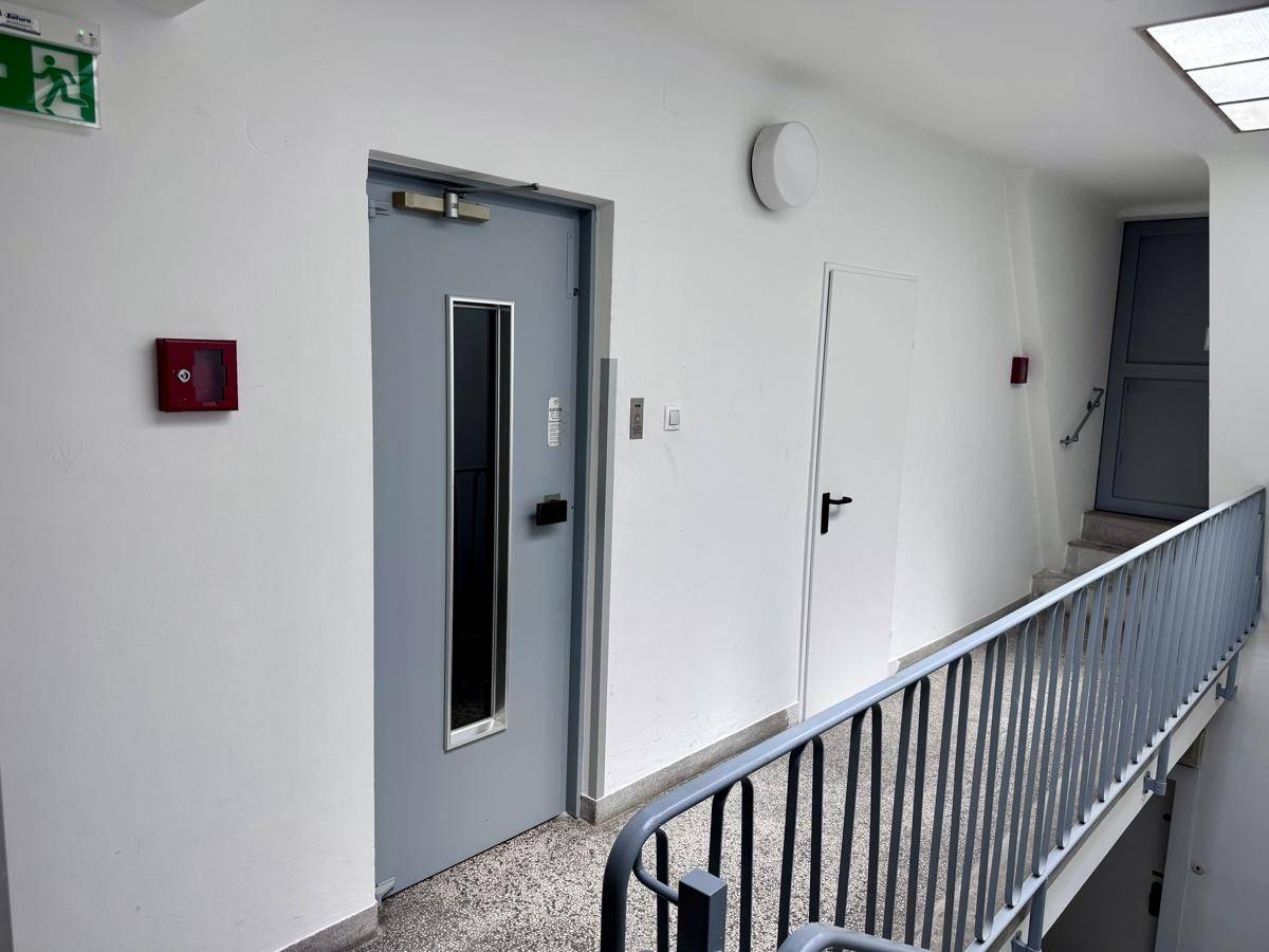 Gemeinschaftlicher Treppenhausbereich mit grauem Geländer und Aufzugstür.