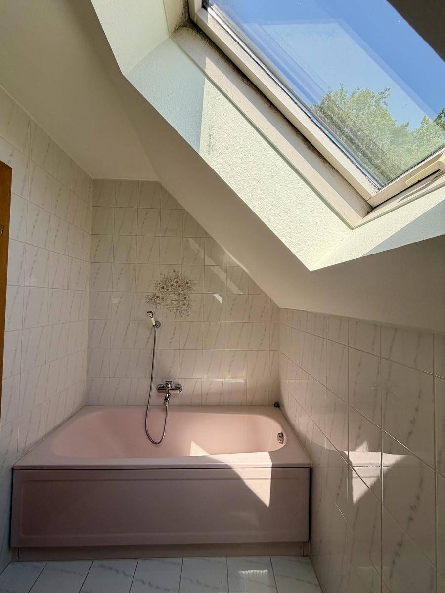 Badezimmer im Dachgeschoss mit Badewanne und Dachfenster, in einem älteren Stil gehalten.