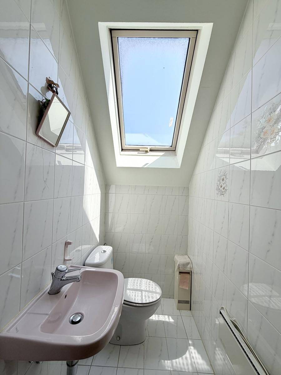 Kleines WC mit Waschbecken und Dachfenster, komplett gefliest und hell.