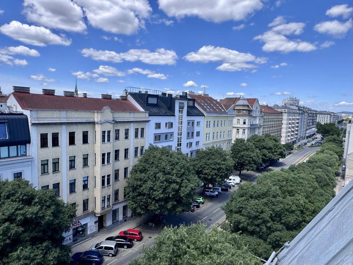 Panoramablick über eine belebte Stadtstraße mit Gebäuden, Bäumen und parkenden Autos.