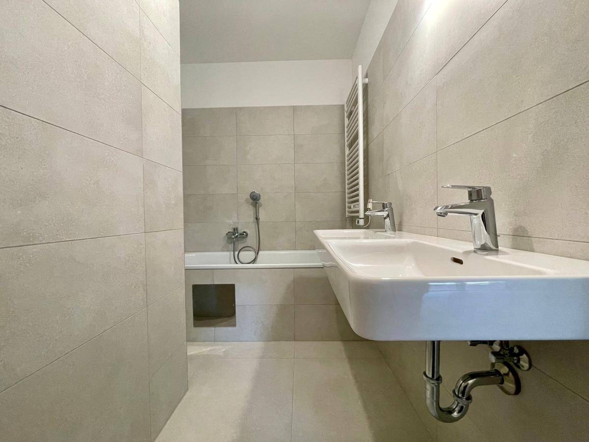 Modernes Badezimmer mit hellgrauen Fliesen, Badewanne und einem einzelnen Waschbecken.