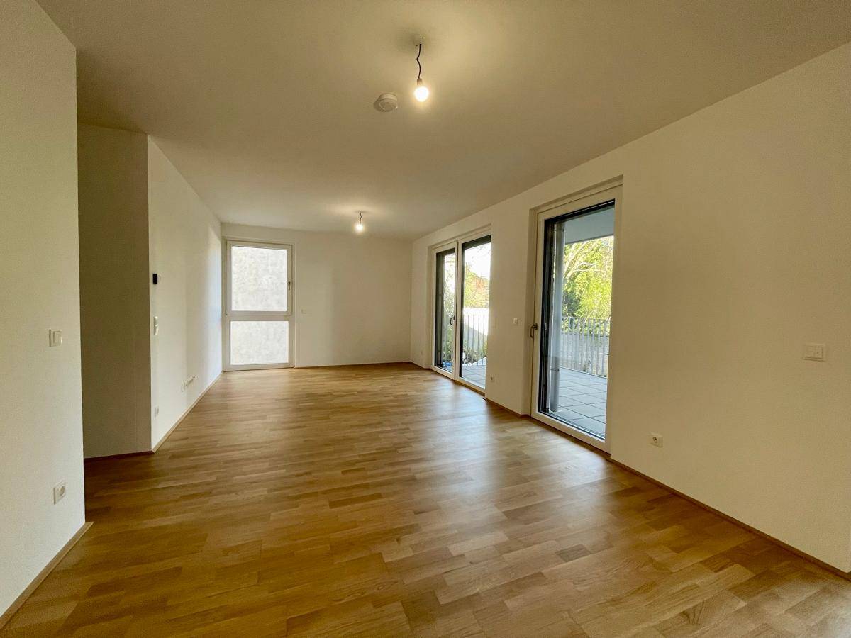 Geräumiger, heller Wohnbereich mit Holzboden und mehreren Fenstern, die viel Tageslicht hereinlassen.