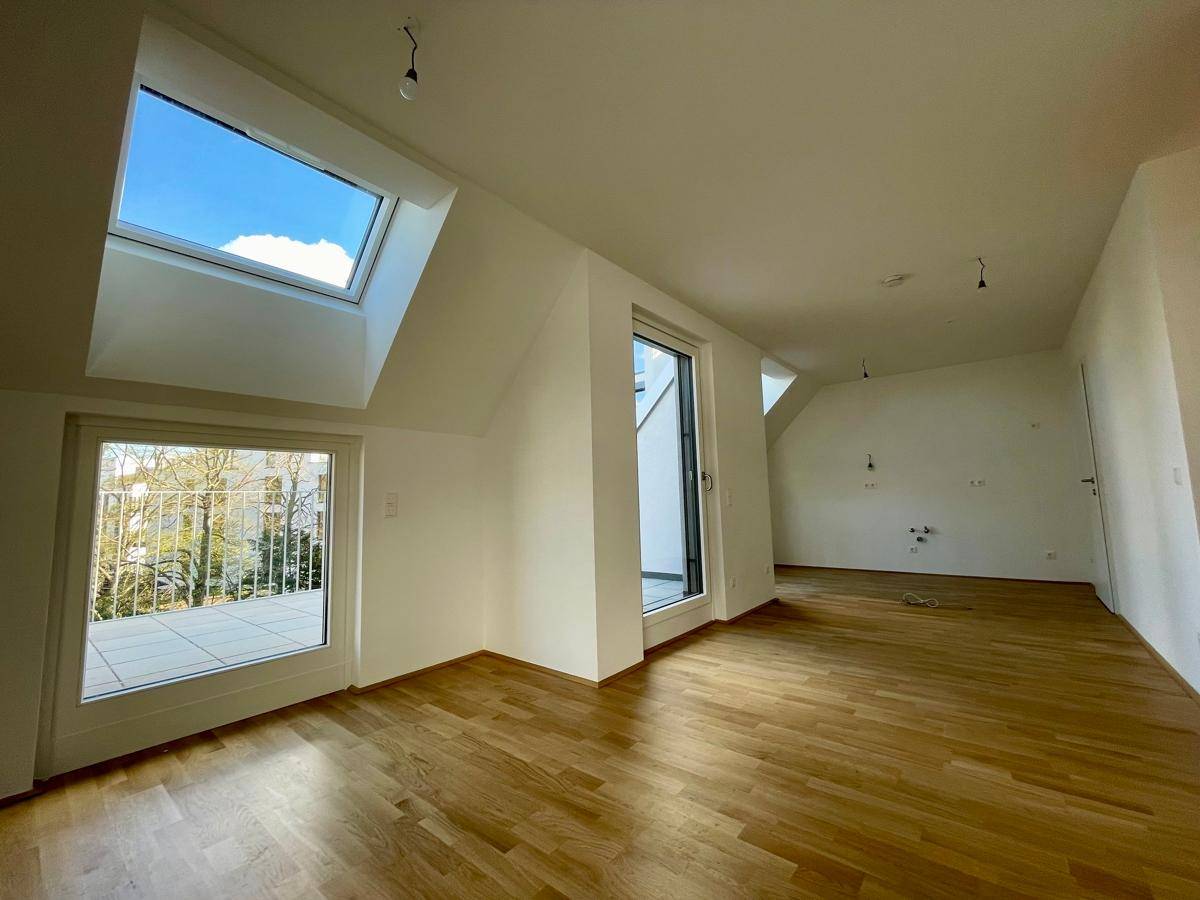 Lichtdurchfluteter Raum mit Holzboden, Dachfenstern und Zugang zu einer großzügigen Terrasse.