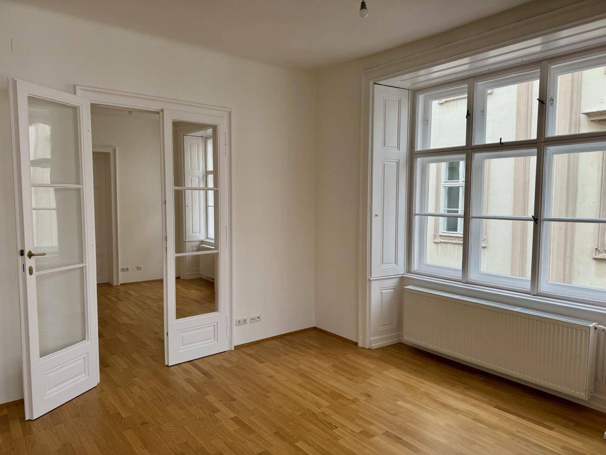Heller Raum mit Holzboden, großen Fenstern und weißen Wänden, bereit zur Einrichtung.