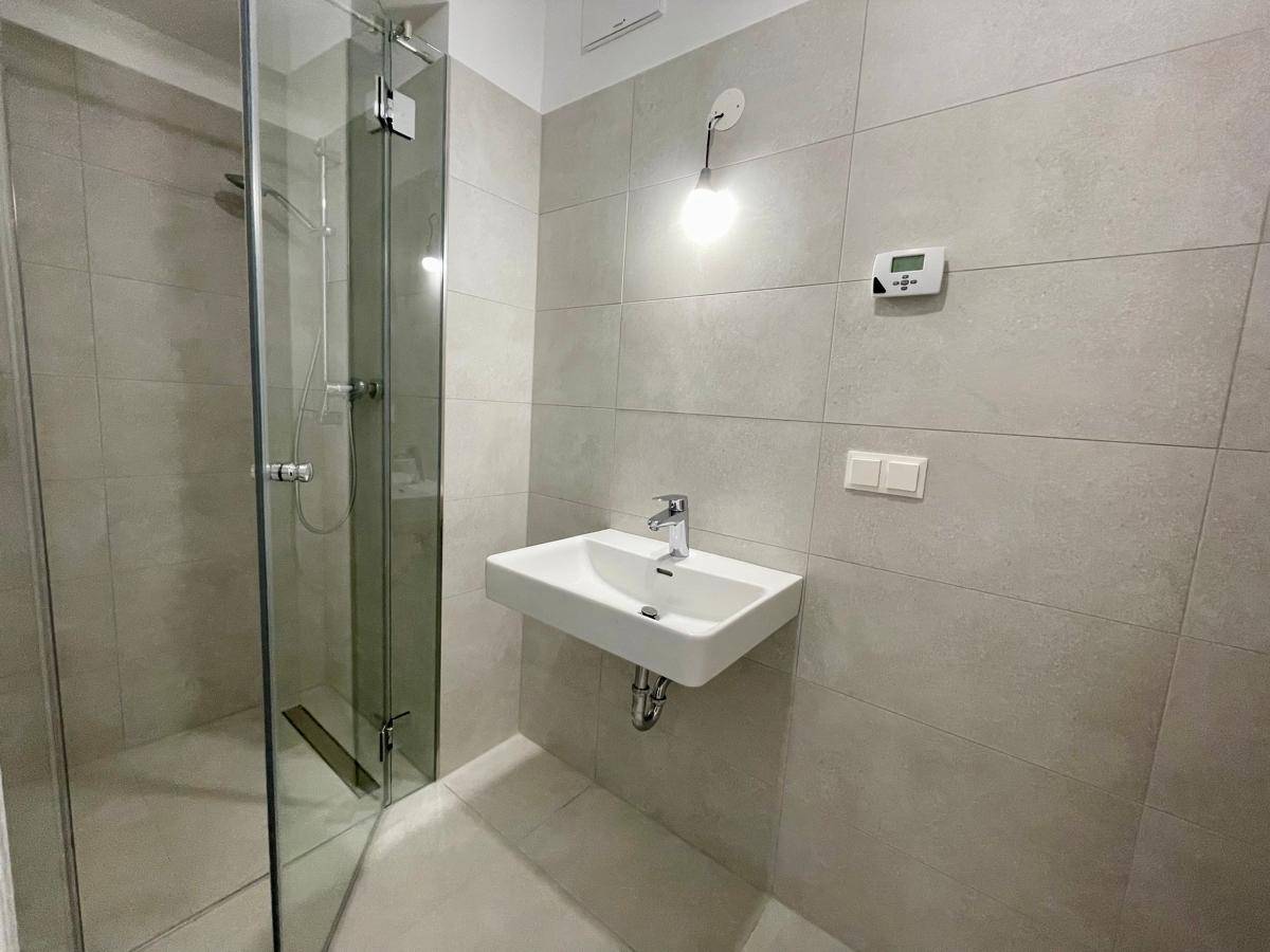 Modernes Badezimmer mit ebenerdiger Dusche, Einzelwaschbecken und hellgrauen Fliesen.
