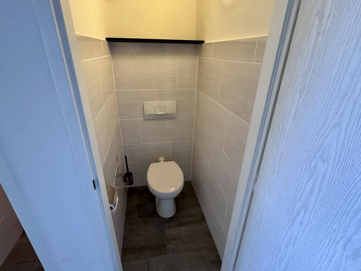 Separates WC mit wandhängender Toilette und modernen grauen Fliesen.