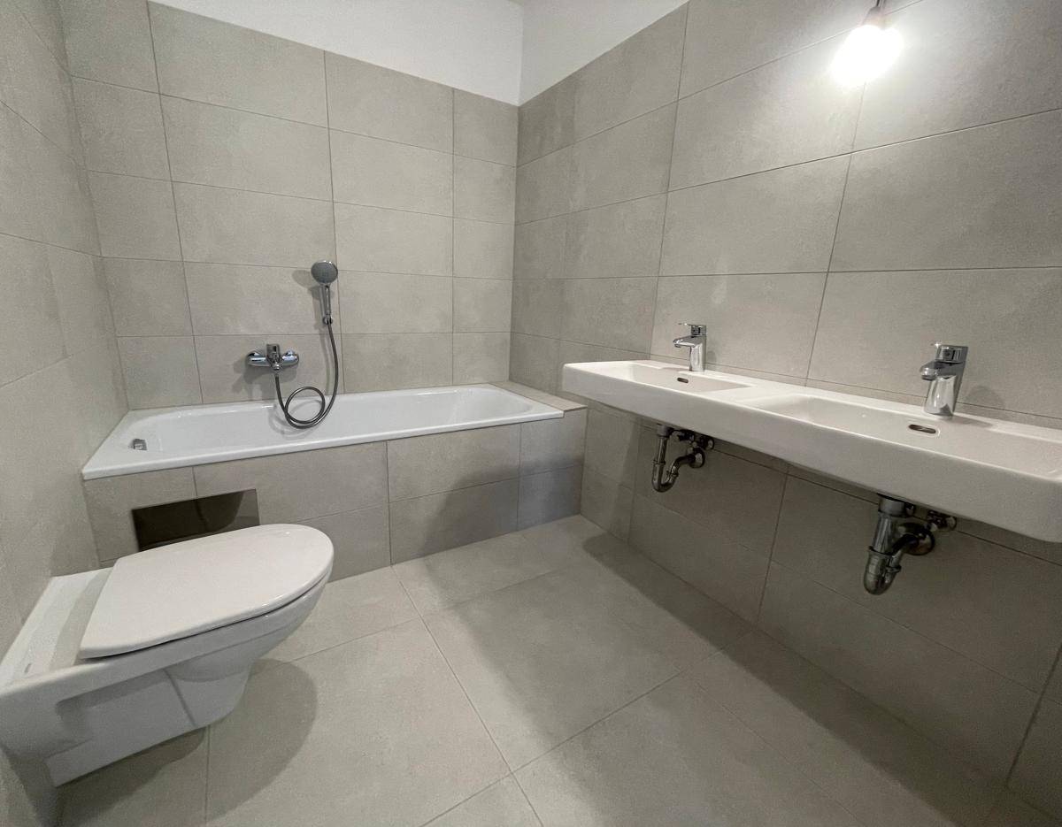 Modernes Badezimmer mit hellgrauen Fliesen, Badewanne, Doppelwaschbecken und Wand-WC.