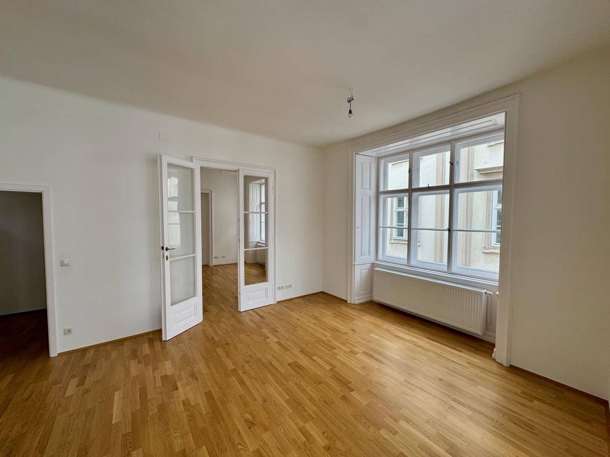 Geräumiger, heller Raum mit Holzboden und hohen Fenstern, ideal für Wohn- oder Arbeitszwecke.