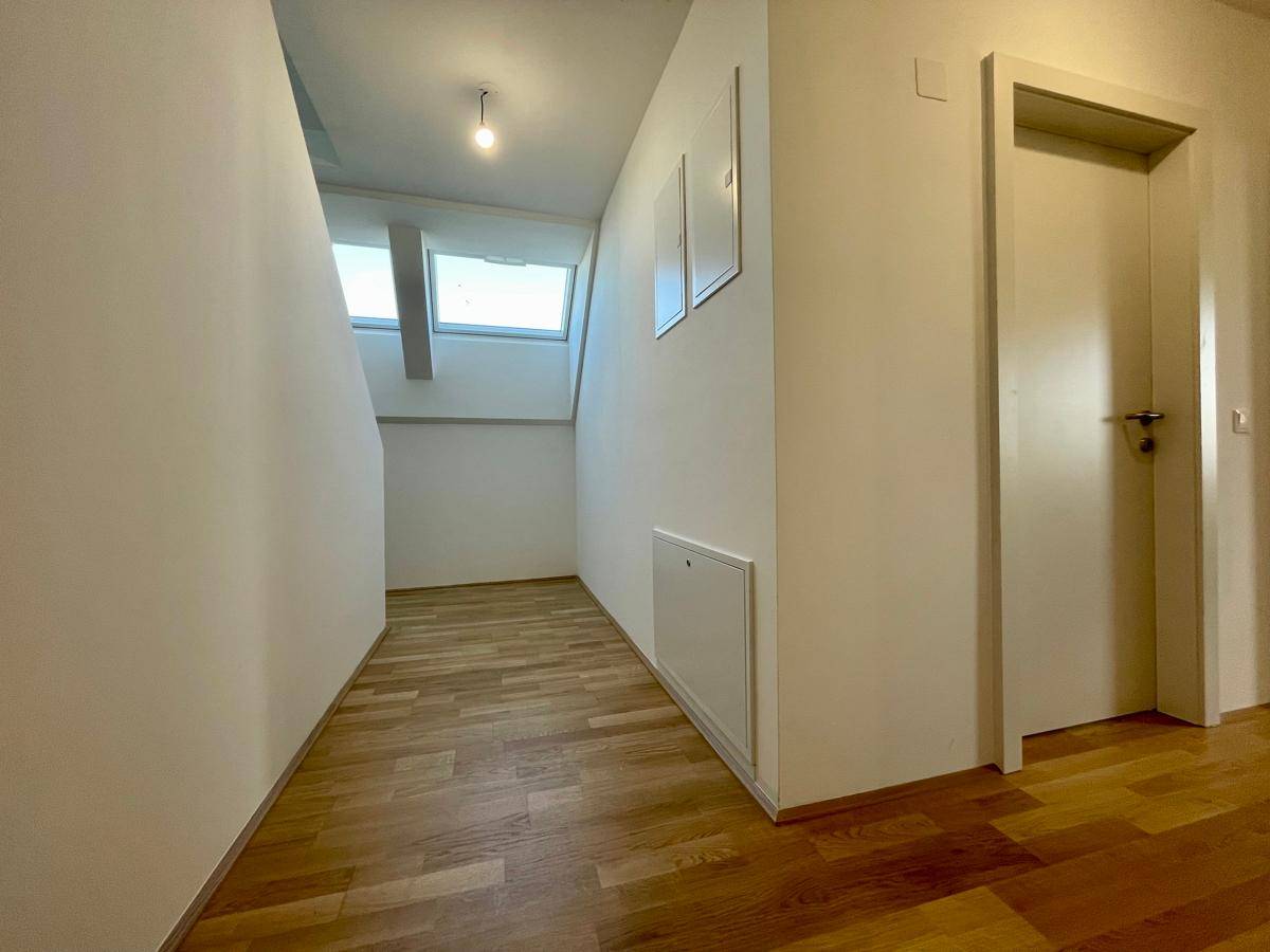 Heller Flur mit Holzparkettboden und schrägen Wänden, beleuchtet durch Dachfenster.