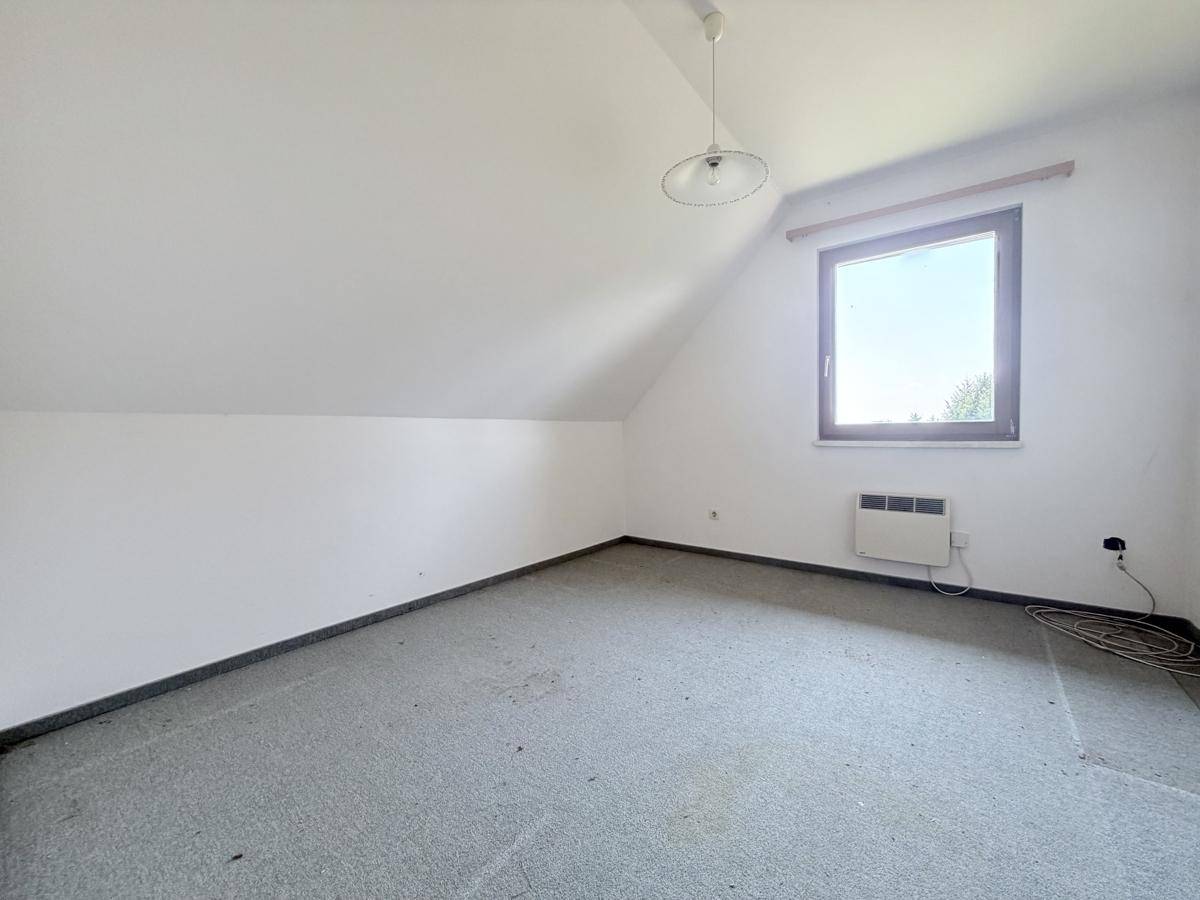 Helles Dachzimmer mit schräger Decke und Fenster, bietet eine ruhige Atmosphäre.