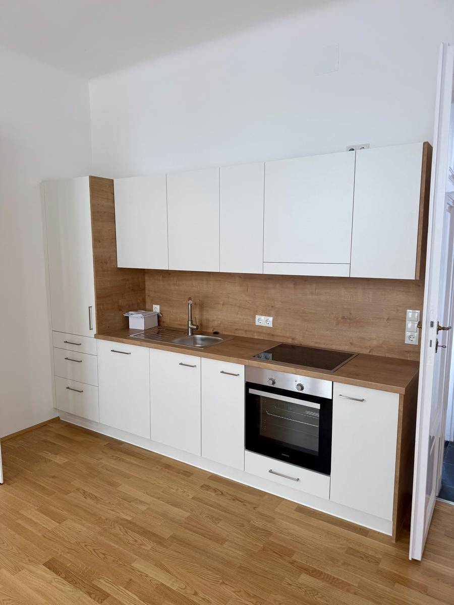 Moderne Einbauküche mit weißen Schränken, Holzdetails und integrierten Elektrogeräten.