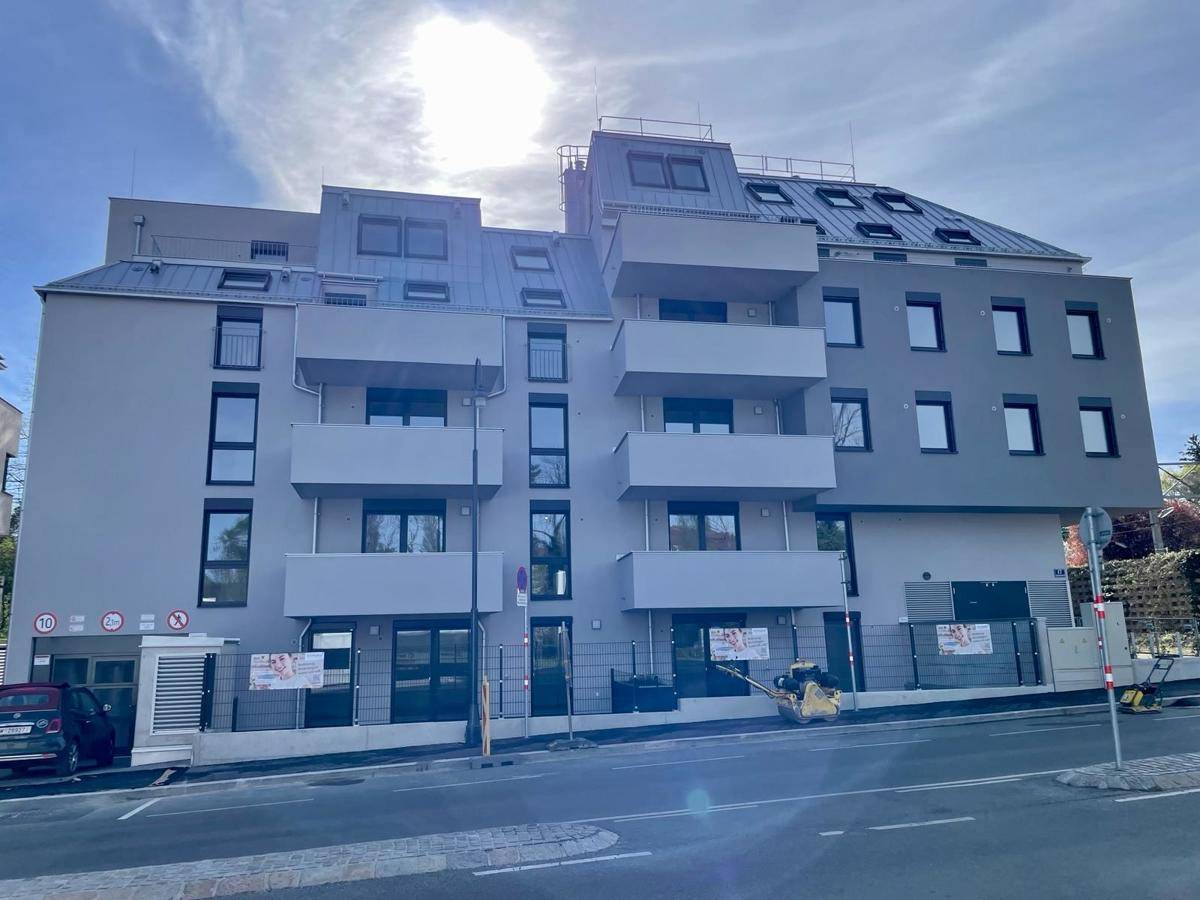 Neubau-Fassade mit mehreren Balkonen und Dachfenstern an einem sonnigen Tag.