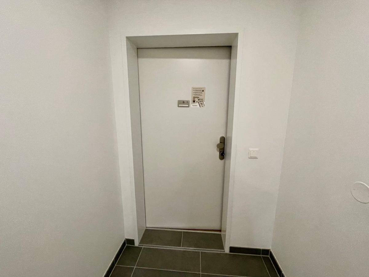 Schlichter Flur mit weißer Tür und dunklen Bodenfliesen, der den Eingangsbereich kennzeichnet.