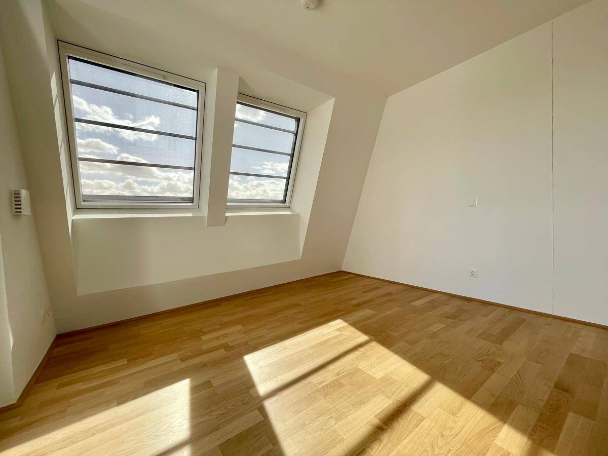 Helles Schlafzimmer mit Holzparkettboden und zwei Dachfenstern unter schräger Decke.